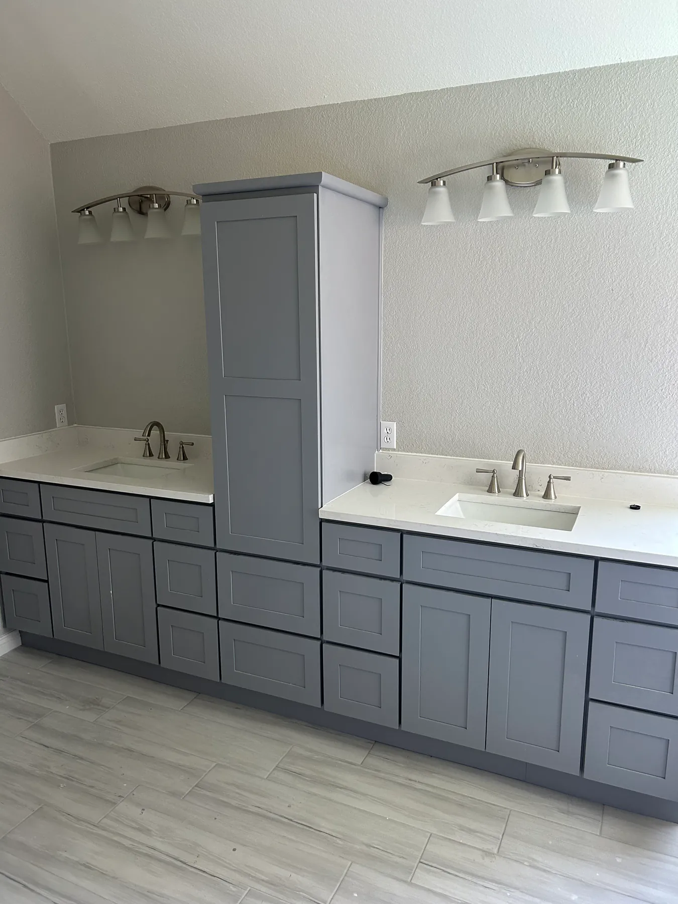 A finished bathroom remodel: grey shaker double vanity, white quartz countertops with undermount sinks, and wood-look plank tile flooring