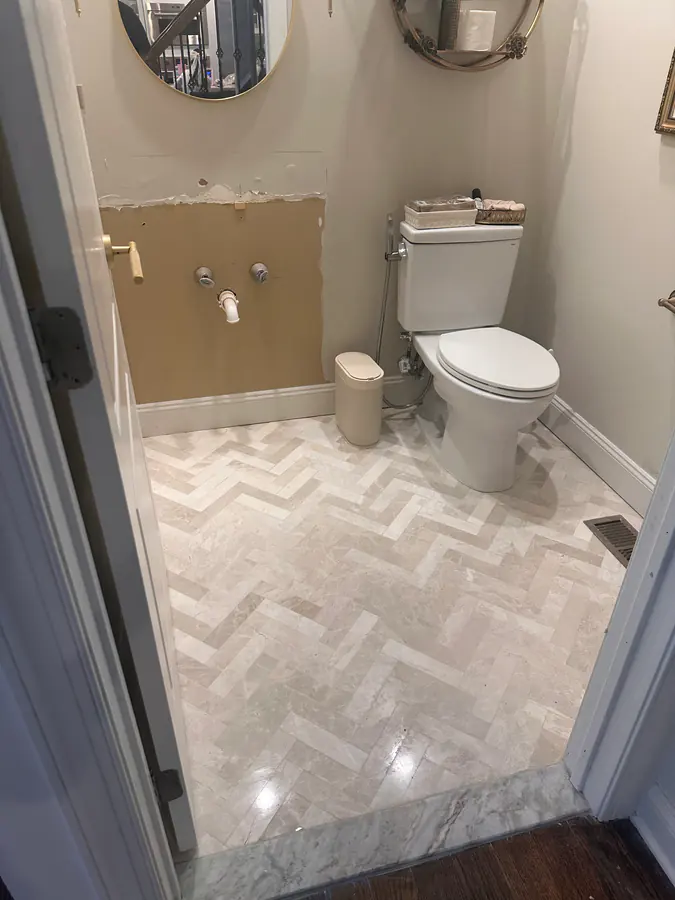 Herringbone marble tile floor in a powder room remodel, cut clean to the baseboard on every side