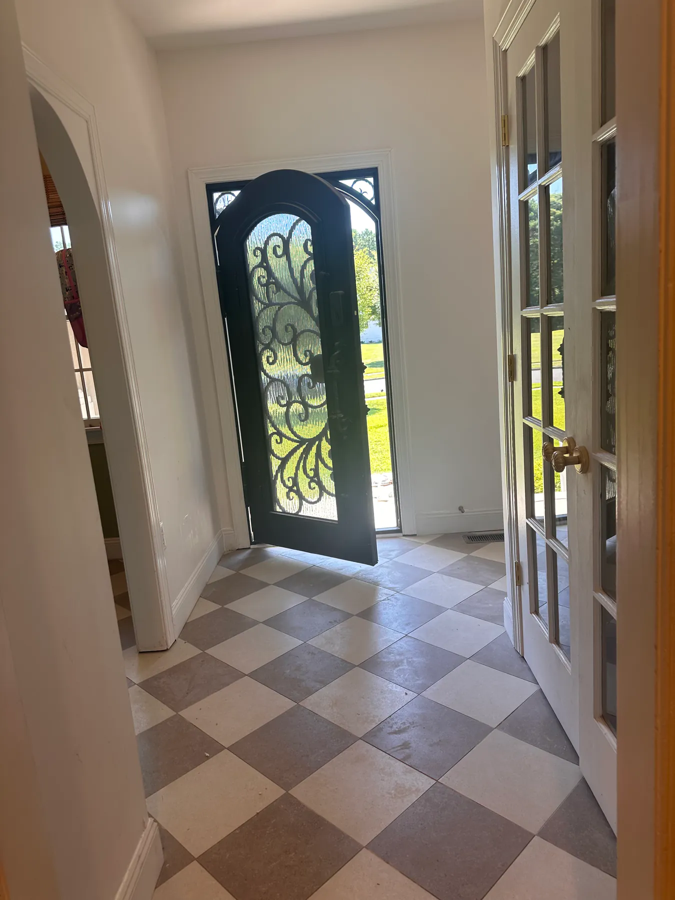 Entryway with a checkerboard travertine tile floor laid on the diagonal beneath an arched iron door