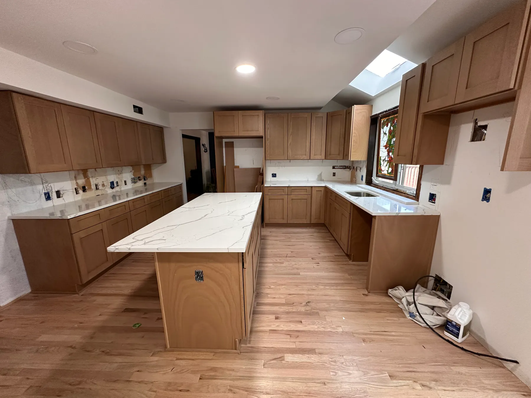 Kitchen remodel with a calacatta-pattern quartz island set on newly laid red oak hardwood flooring