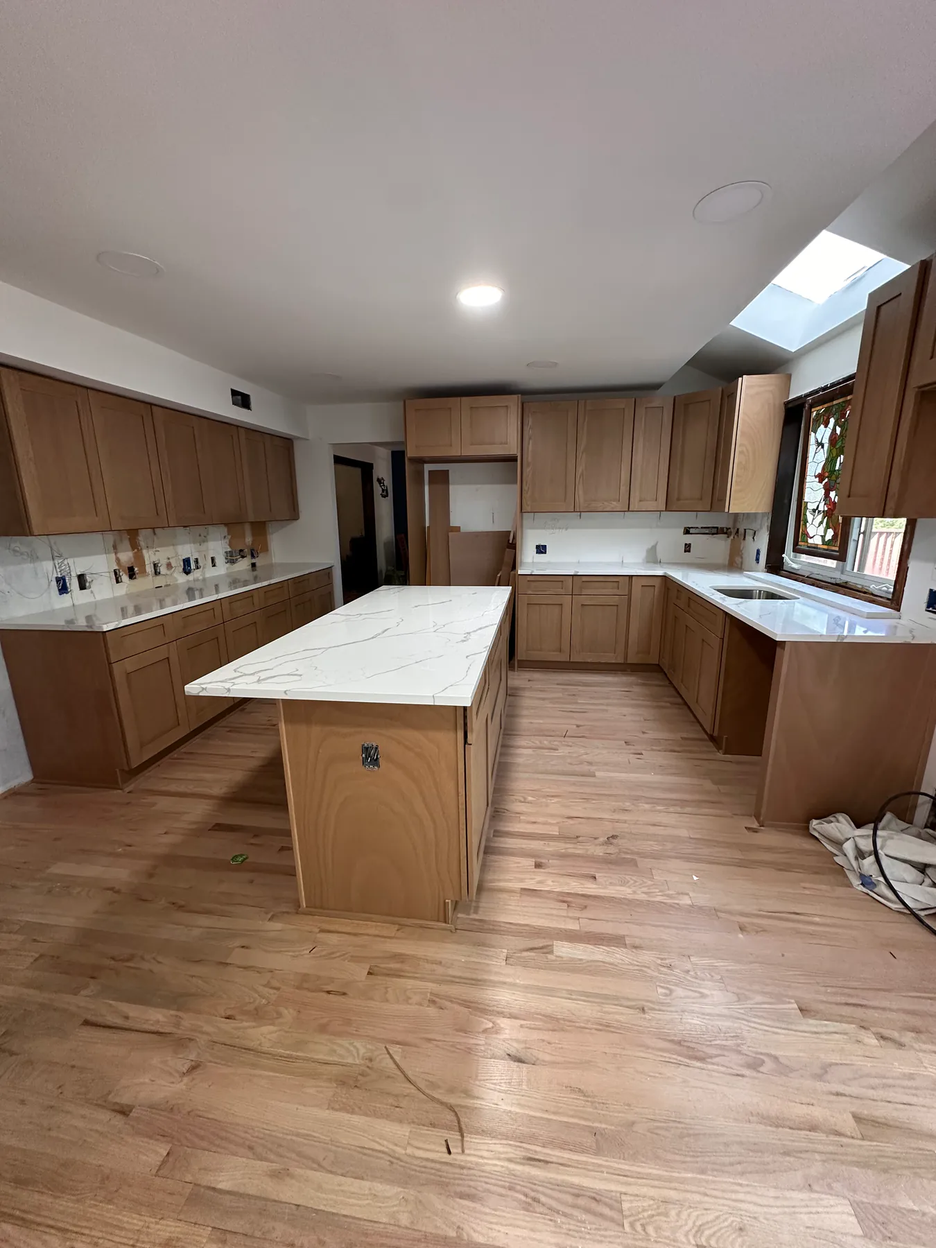 White oak shaker cabinets and a quartz island in a kitchen remodel, with red oak floor running throughout