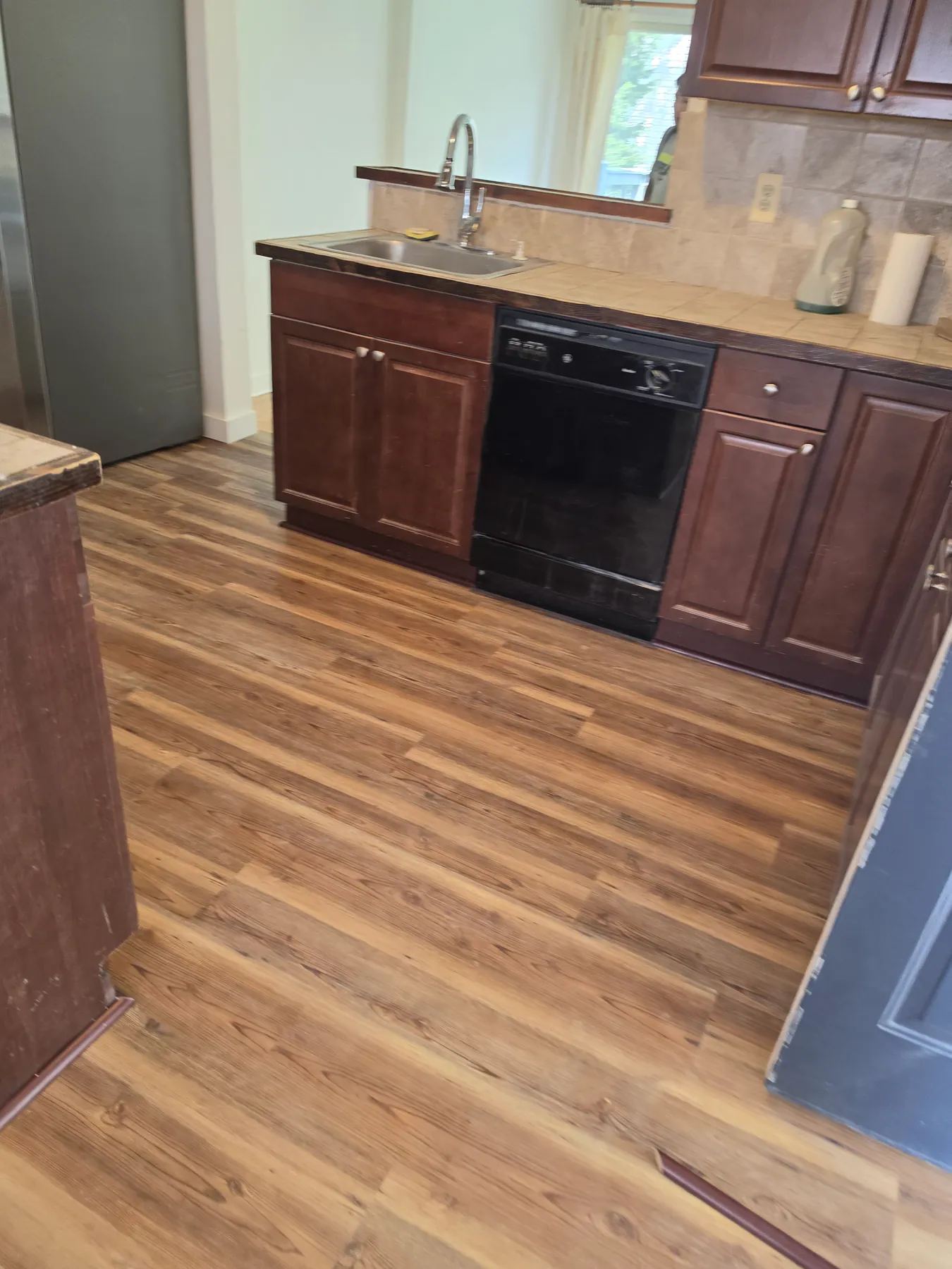 Luxury vinyl plank floor in a kitchen with dark cherry cabinets and a tiled backsplash