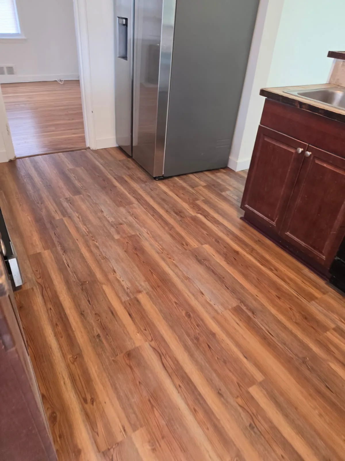Honey oak vinyl plank flooring running the length of a kitchen past the refrigerator