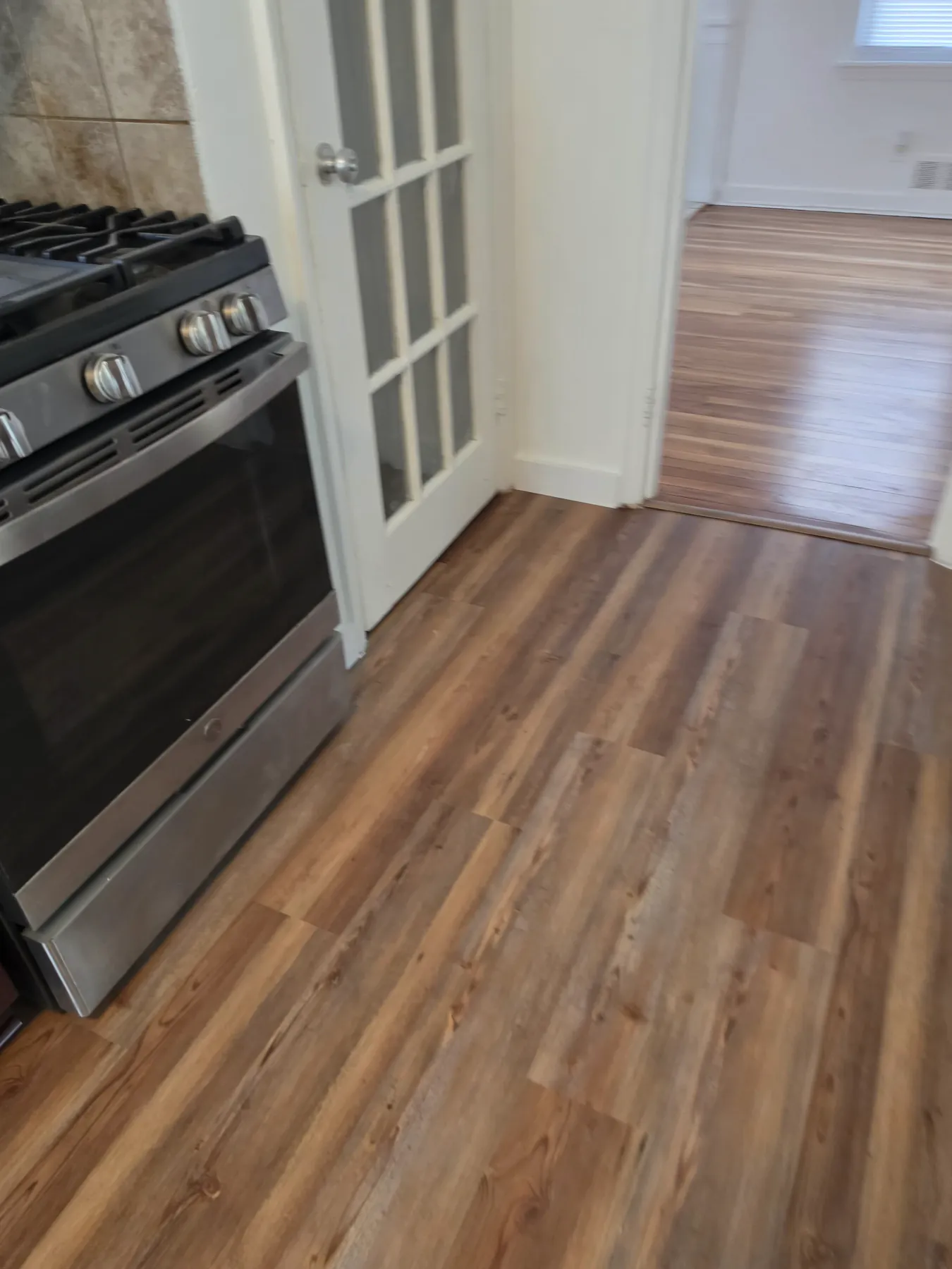Luxury vinyl plank flooring laid past a gas range and through a french door opening